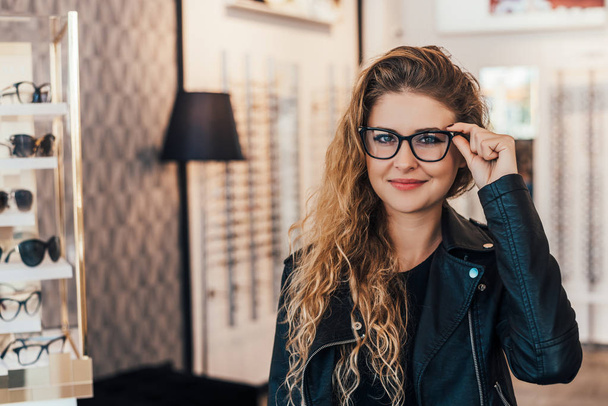 young woman choosing new glasses frames in optician store - Zdjęcie, obraz