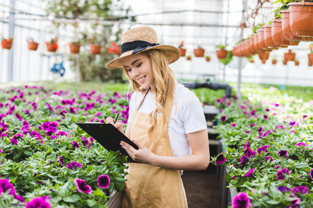 Young female owner of glasshouse with clipboard filling order of flowers - Photo, Image