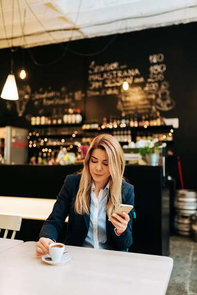 Businesswoman drinking coffee and using smartphone in restaurant - Photo, image