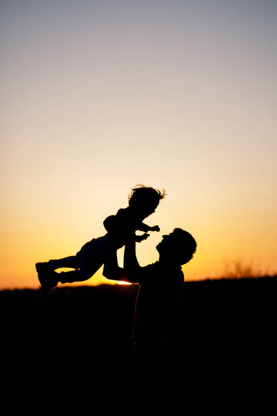 Silueta muže a jeho syn hrát spolu venkovní při západu slunce. Vertikální fotografie. Koncepce - Fotografie, Obrázek