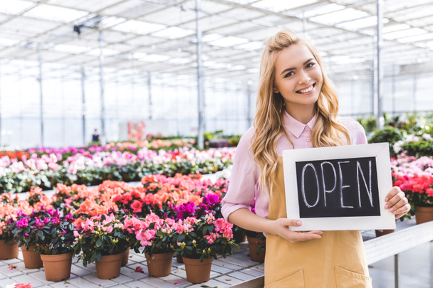 Blonde woman holding Open board by flowers in greenhouse - Foto, afbeelding
