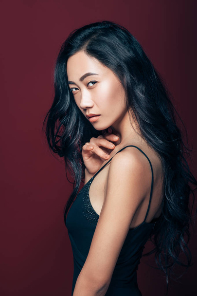 Beautiful asian woman in black dress posing in studio on brown background. Pretty fashion model portrait - Фото, изображение