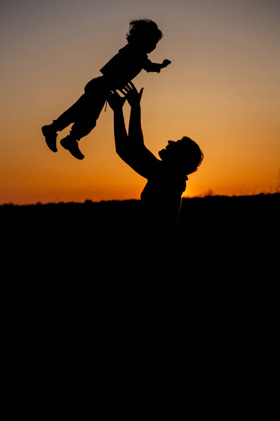Loving father and his little son having fan together outdoors. Happy family. Fatherhood. Toddler boy and his dad playing. Family as silhouette on sunset. Vertical photo - Foto, imagen