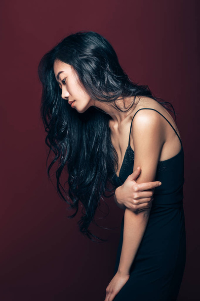 Profile portrait of beautiful asian woman in black dress posing in studio on brown background. Pretty fashion model portrait - Fotó, kép