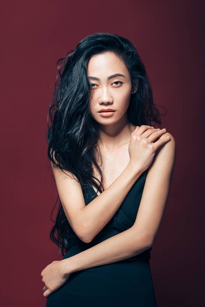 Beautiful asian woman in black dress posing in studio on brown background. Pretty fashion model portrait - Фото, изображение