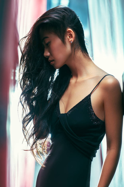 Side view portrait of asian beautiful woman posing, head tilted, look down. Young model in fashion pose, hands along of body, slightly curved, bright background - Foto, Imagem