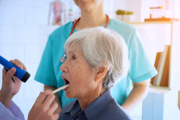 Médico verificando a garganta examinando de mulher idosa com lanterna
 - Foto, Imagem