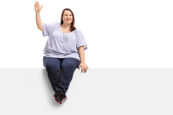 Overweight woman sitting on a panel and waving at the camera isolated on white background - Zdjęcie, obraz