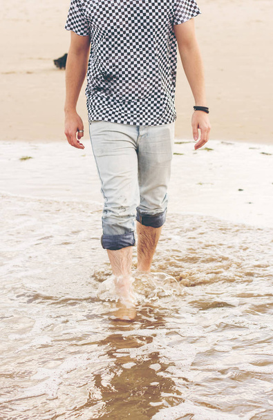 若い男が砂浜の上を歩いて作物 - 写真・画像