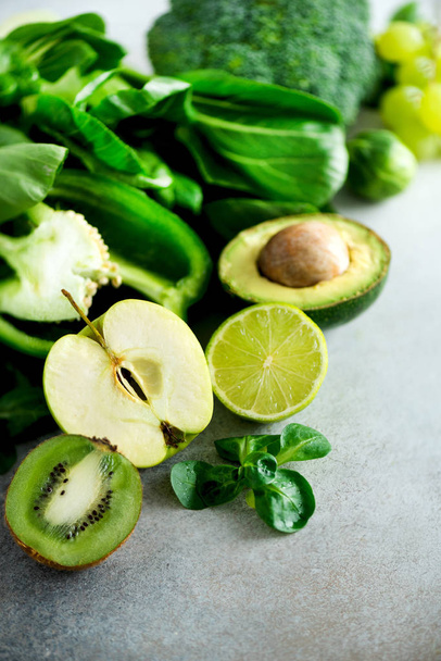 Organic green vegetables and fruits on grey background. Copy space. Green apple, lettuce, cucumber, avocado, kale, lime, kiwi, grapes, banana, broccoli - Foto, Bild