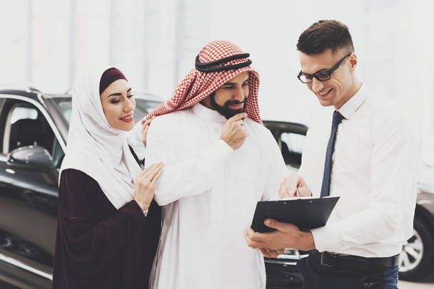 salesman help choosing new auto to Arabic couple at car dealership - Фото, изображение