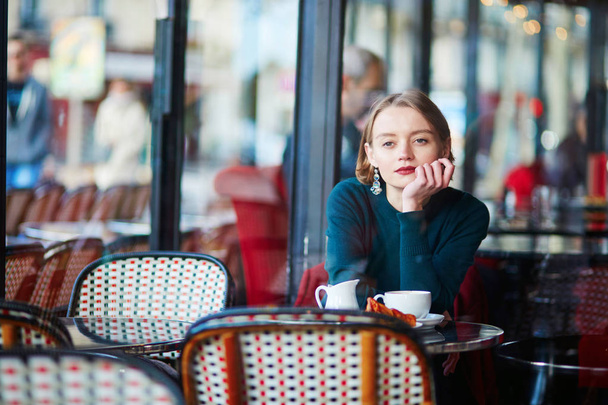 Young elegant woman drinking coffee and using her mobile phone in traditional cafe in Paris, France - Foto, Imagem
