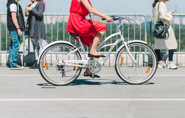 Uma senhora de bicicleta. A menina no vestido vermelho andando de bicicleta pela cidade. Um passeio de bicicleta na cidade no fundo das pessoas
 - Foto, Imagem
