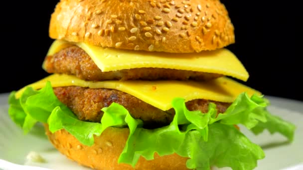 Velký hamburger s masem a sýrem se otočí na talíři - Záběry, video