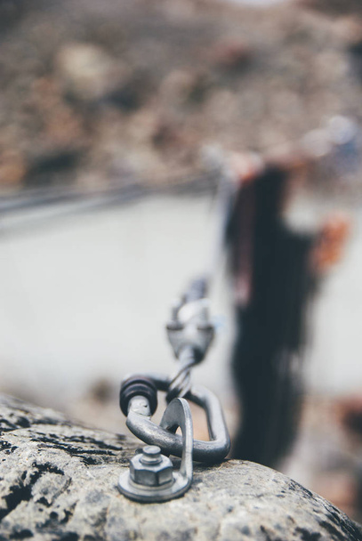 Eisen gedrehtes Seil, das zwischen Felsen gespannt wird, um Klettersteige zu besteigen. Seil im Block durch Schrauben Karabinerhaken befestigt. Detail des Seilenden in Sandsteinfelsen verankert. Geringe Schärfentiefe. - Foto, Bild