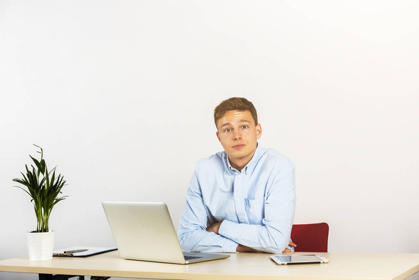 Szczęśliwy młody biznesmen korzysta z laptopa na jego biurku w biurze i uśmiechnięty, spójrz prosto przed siebie. - Zdjęcie, obraz