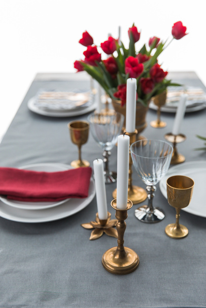 selective focus of candles in vintage candle holders, bouquet of red tulips and arranged empty plates on tabletop - Photo, Image