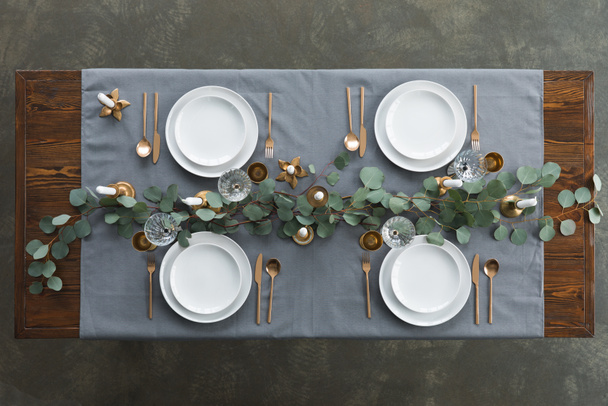 top view of rustic table setting with eucalyptus, tarnished cutlery, wine glasses, candles and empty plates on tabletop - Photo, Image