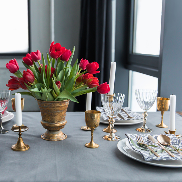 close up view of bouquet of red tulips on tabletop with arranged vintage cutlery and candles - Foto, Imagem