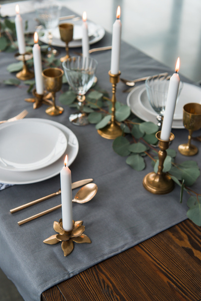close up view of rustic table arrangement with eucalyptus, vintage cutlery, candles in candle holders and empty plates - Photo, Image