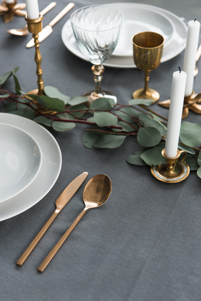 vue rapprochée de la disposition rustique de la table avec eucalyptus, couverts vintage, bougies dans des bougeoirs et des assiettes vides
 - Photo, image