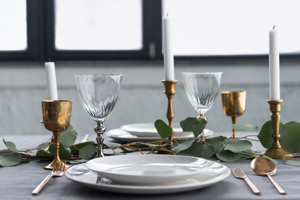 Close-up beeld van de instelling van de rustieke tabel met wijnglazen, eucalyptus, vintage bestek, kaarsen in Kaarsenbakjes en lege platen - Foto, afbeelding