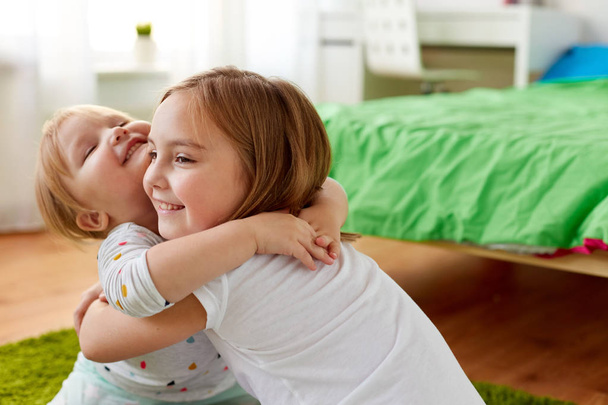 happy little girls or sisters hugging at home - Φωτογραφία, εικόνα