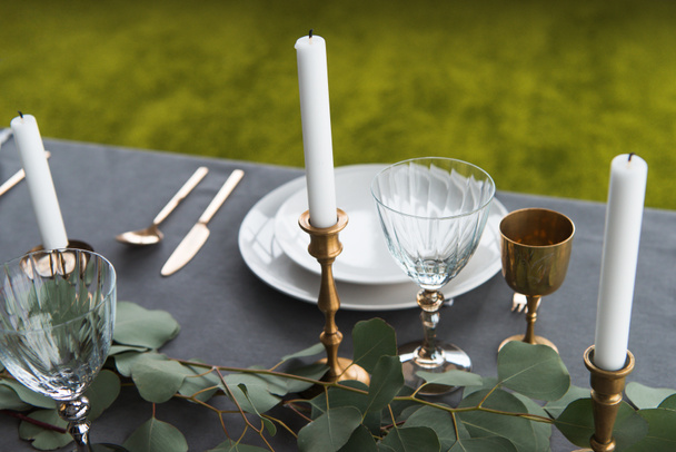 vista de cerca de la mesa rústica con copas de vino, eucalipto, cubiertos a la antigua, velas en candelabros y platos vacíos
 - Foto, Imagen