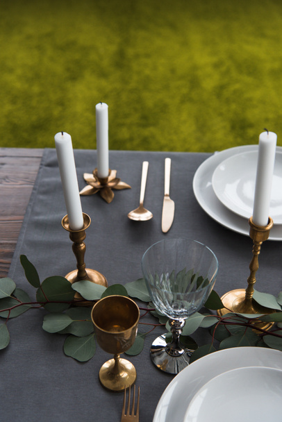 close up view of rustic table arrangement with winecups, eucalyptus, vintage cutlery, candles in candle holders and empty plates - Photo, Image