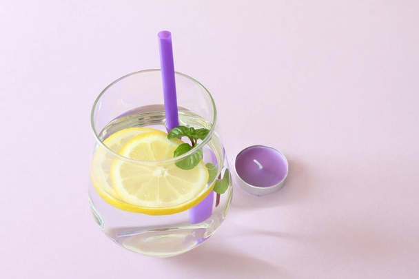 水、レモン、ミント、キャンドルのガラス。純粋な水と新鮮なオーガニック レモンとミントの紫色の背景と紫のロウソクに分離のガラス。デトックスと健康食品のコンセプト - 写真・画像