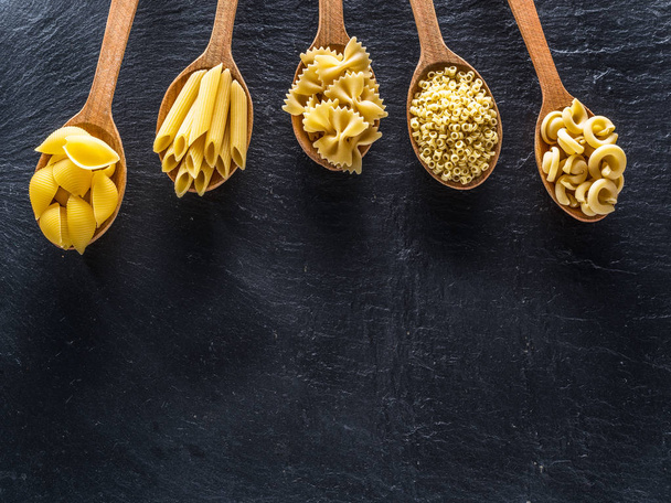 Different pasta types in wooden spoons on the table. Top view. - 写真・画像