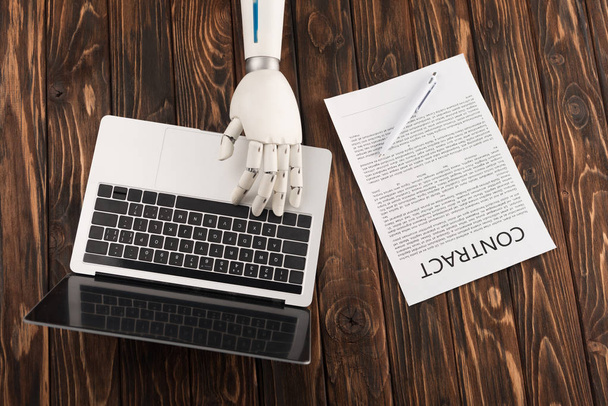 Oříznout záběr robota pracovat s notebookem na dřevěný povrch s obchodní kontrakt - Fotografie, Obrázek