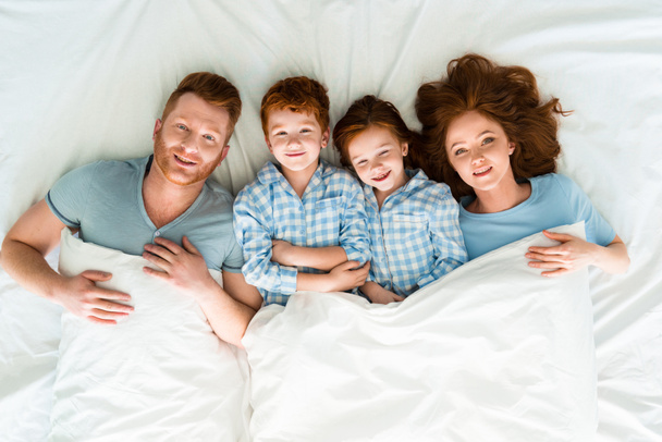 heureux rousse famille en pyjama couché dans le lit et souriant à la caméra
  - Photo, image
