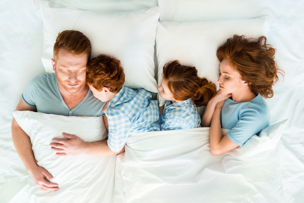ベッドで一緒に寝ている二人の子供連れのご家族 - 写真・画像