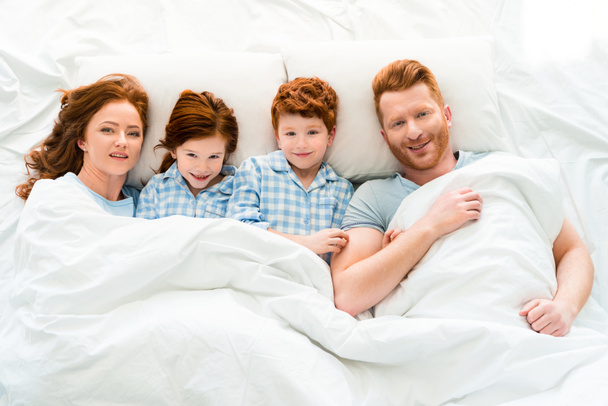 gelukkige familie in pyjama in bed liggen en lachend op camera  - Foto, afbeelding
