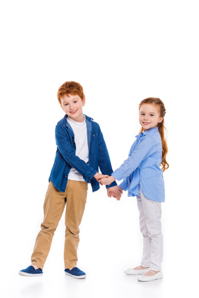 beautiful redhead siblings holding hands and smiling at camera isolated on white - Foto, Imagem