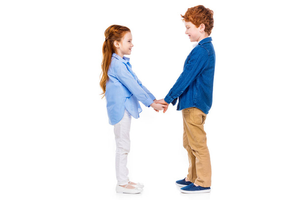 Seitenansicht von niedlichen glücklichen Kindern, die sich an den Händen halten und einander isoliert auf weiß lächeln - Foto, Bild