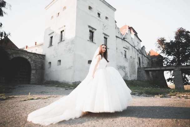 Beautiful elegant bride with perfect wedding dress and bouquet posing near old castle - 写真・画像