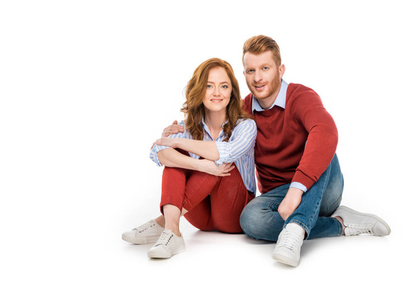 beautiful happy redhead couple sitting together and smiling at camera isolated on white  - Φωτογραφία, εικόνα