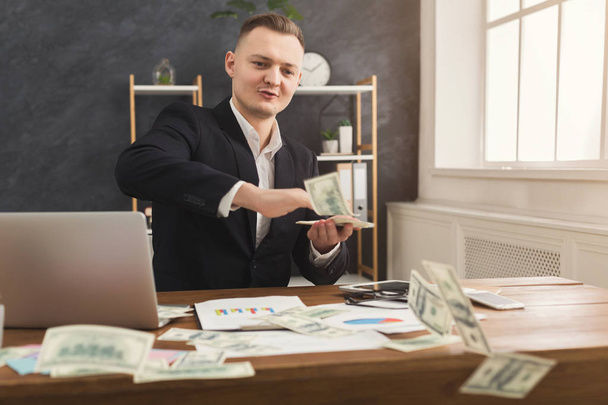 Χρηματοδότης άνθρωπος κάθεται στο γραφείο και να κατέχουν χρήματα στο χέρι - Φωτογραφία, εικόνα