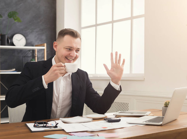 Fiatal férfi manager beszélgetni a laptop, és kávét iszik - Fotó, kép