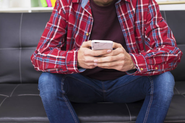adulto joven con teléfono móvil en el sofá de la casa o apartamento
 - Foto, Imagen