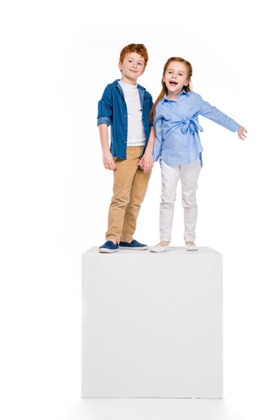 cute happy children standing on white cube and smiling at camera isolated on white - Photo, Image