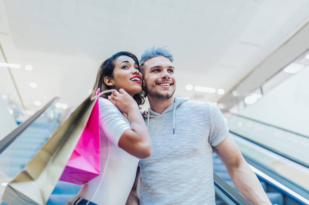  glückliches junges Paar mit Einkaufstüten spazieren in Einkaufszentrum - Verkauf, Konsum und Menschen-Konzept  - Foto, Bild