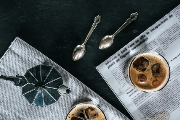 tumbado plano con cafetera, cucharas, periódico y vasos de café elaborado en frío sobre una mesa negra
 - Foto, imagen