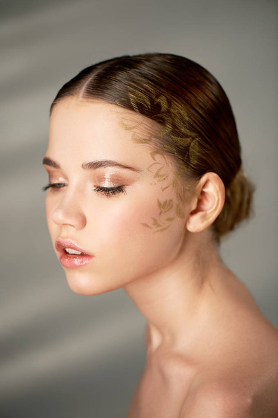 Portrait of young beautiful girl in Studio, with professional makeup. Beauty shooting.On the face pattern gold, sprayed through a stencil. Clear skin.Beauty shooting, - Fotoğraf, Görsel