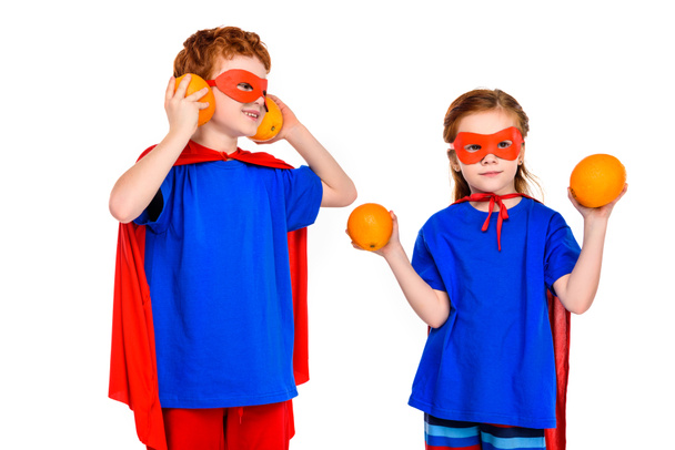 cute super children in masks and cloaks holding oranges isolated on white - Foto, afbeelding