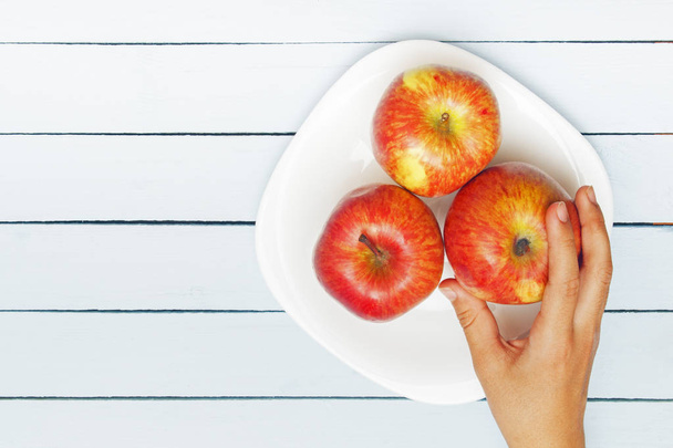 Apples on white plate. Female hand grabing apple. Copy space. Top view - Fotó, kép