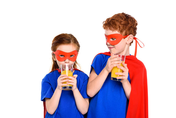 adorable little children in superhero costumes drinking juice isolated on white - 写真・画像
