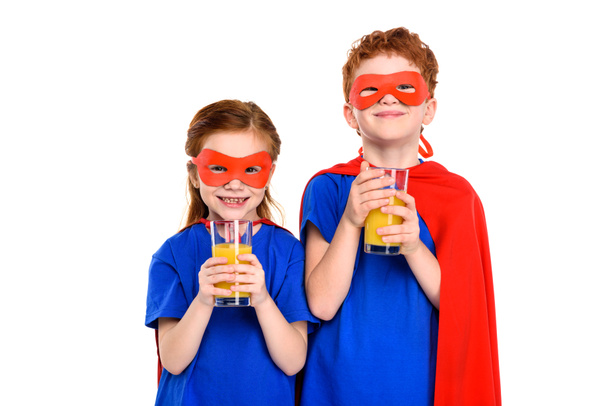 スーパー ヒーロー衣装ジュースのガラスを押しながら白で隔離のカメラに笑顔で幸せな子供たち - 写真・画像